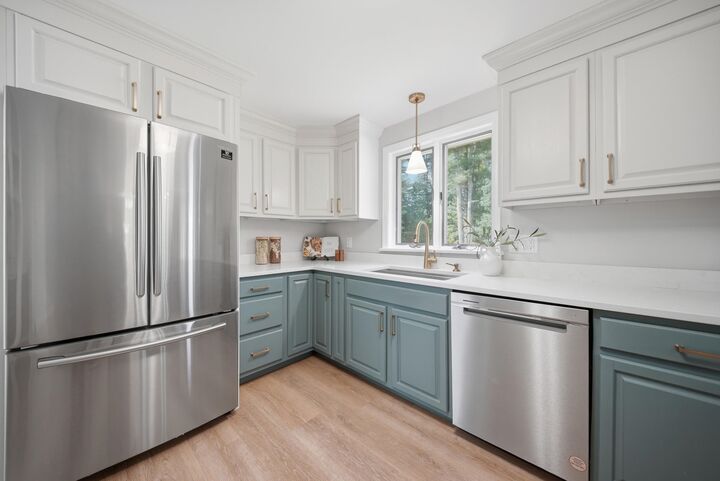 Kitchen with white upper cabinets, blue-green lower cabinets, and stainless steel appliances at 7 Twin Street, Windham, NH